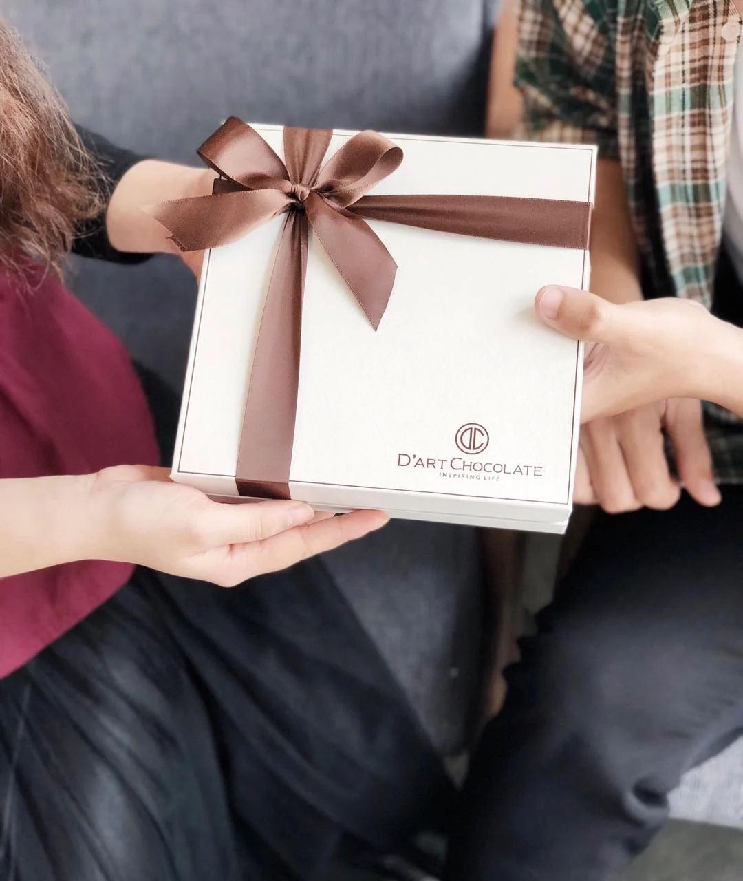 A ribbon-tied D'art gift box passed between two people