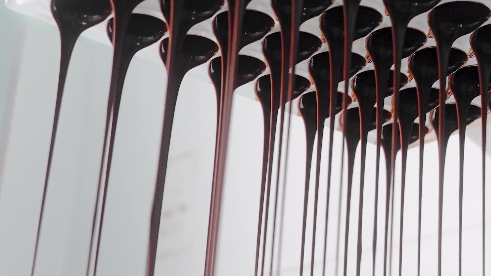 Tempered chocolate draining in long threads from a just-turned bonbon mould