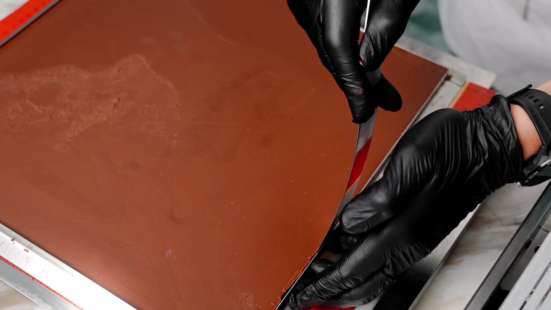 Gloved hands working tempered chocolate on the slab